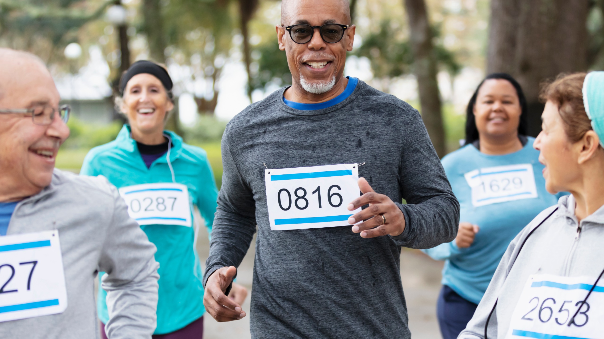 A group of men and women run together, smiling, while wearing race bibs.