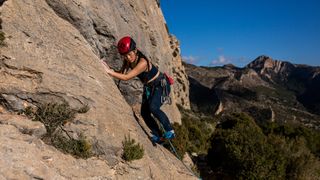 A woman in climbing gear including Unparallel Up Lace climbing shoes carefully makes her way along a rocky mountainside.