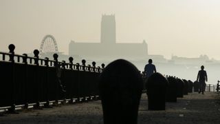 People walk on the Birkenhead promenade with Liverpool Anglican Cathedral on the skyline