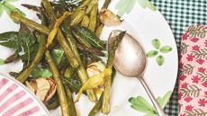 Asparagus garlic and bay leaves on a plate with green and white gingham tablecloth underneath and pink floral napkin next to it