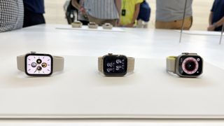 Tre stycken Apple Watch 8 ligger på ett vitt utställningsbord.