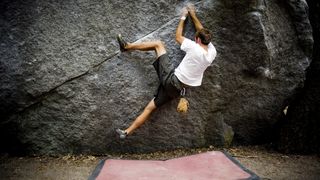 Boulderer climbing above a mat