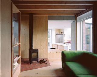 Six Columns House by 31/44 Architects wood burner in wood-lined room, opening onto kitchen