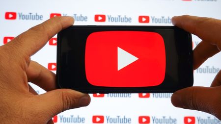 A man holding a smartphone with a Youtube logo and small YouTube logos displayed on a screen are seen in L'Aquila, Italy, on October 9th, 2024. (Photo by Lorenzo Di Cola/NurPhoto via Getty Images)