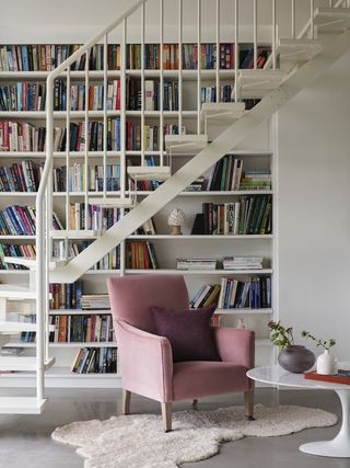 Landing area with bookshelves, staircase, pink armchair and round coffee table