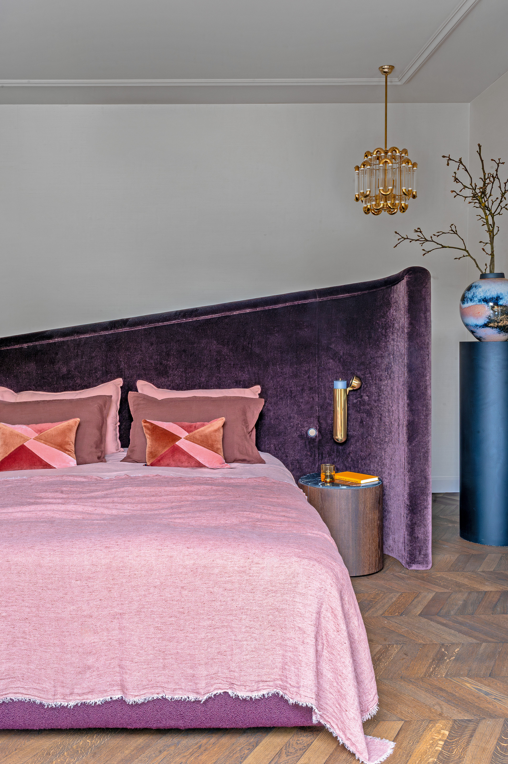 Bedroom with purple velvet angled headboard, pink bed linen and gold chandelier