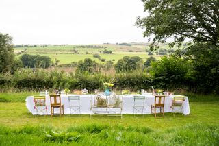 table set for lunch with white cloth and assorted chairs outside with views of fields