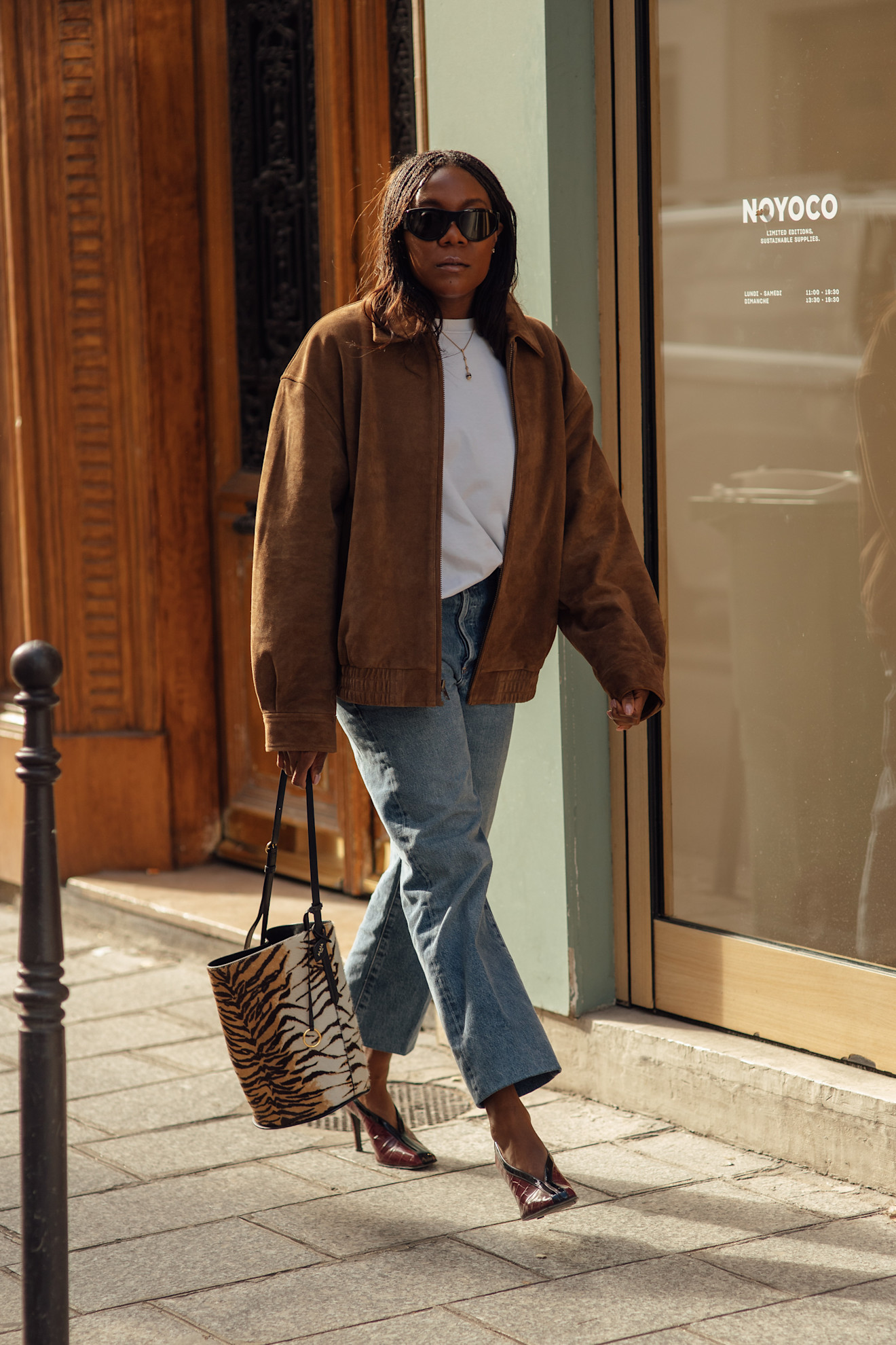 A street style shot of a woman in a suede bomber jacket, jeans, and a zebra print bucket bag