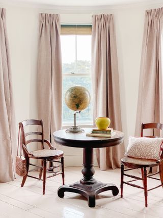 A room with a small table, three large windows with sheer floating curtains