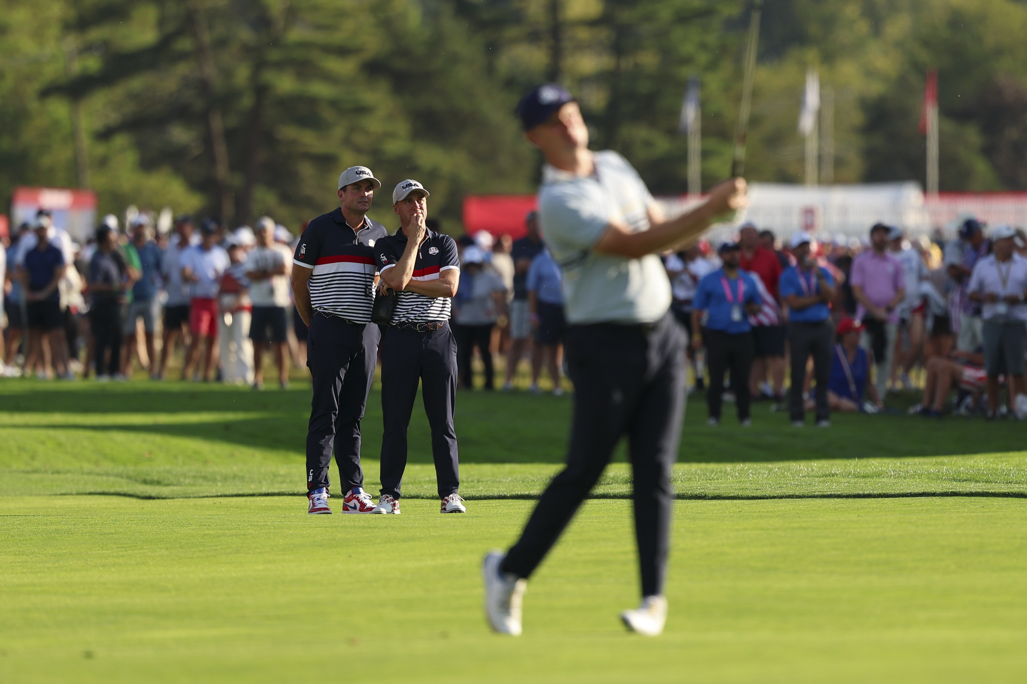 Keegan Bradley and Justin Thomas talk in the background while an out-of-focus Justin Rose hits a shot in the foreground at the 2025 Ryder Cup