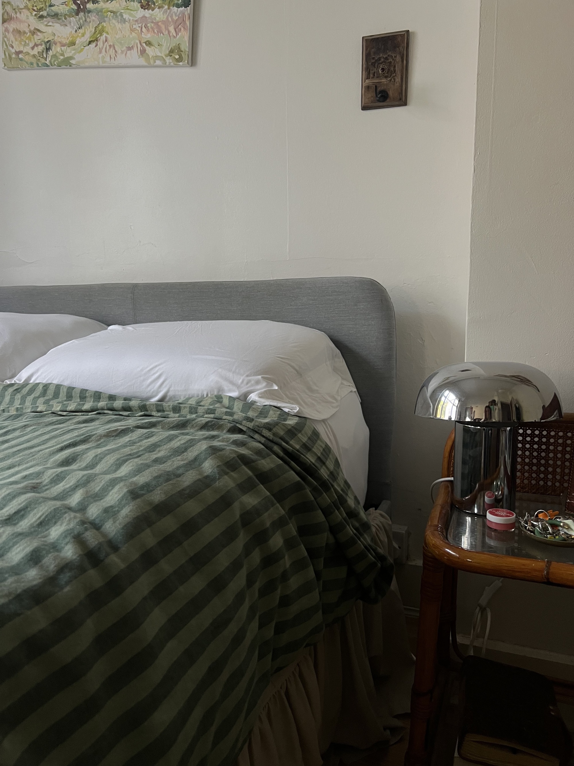 Image of a bed with green striped bedding and a bamboo side table with a chrome mushroom lamp.