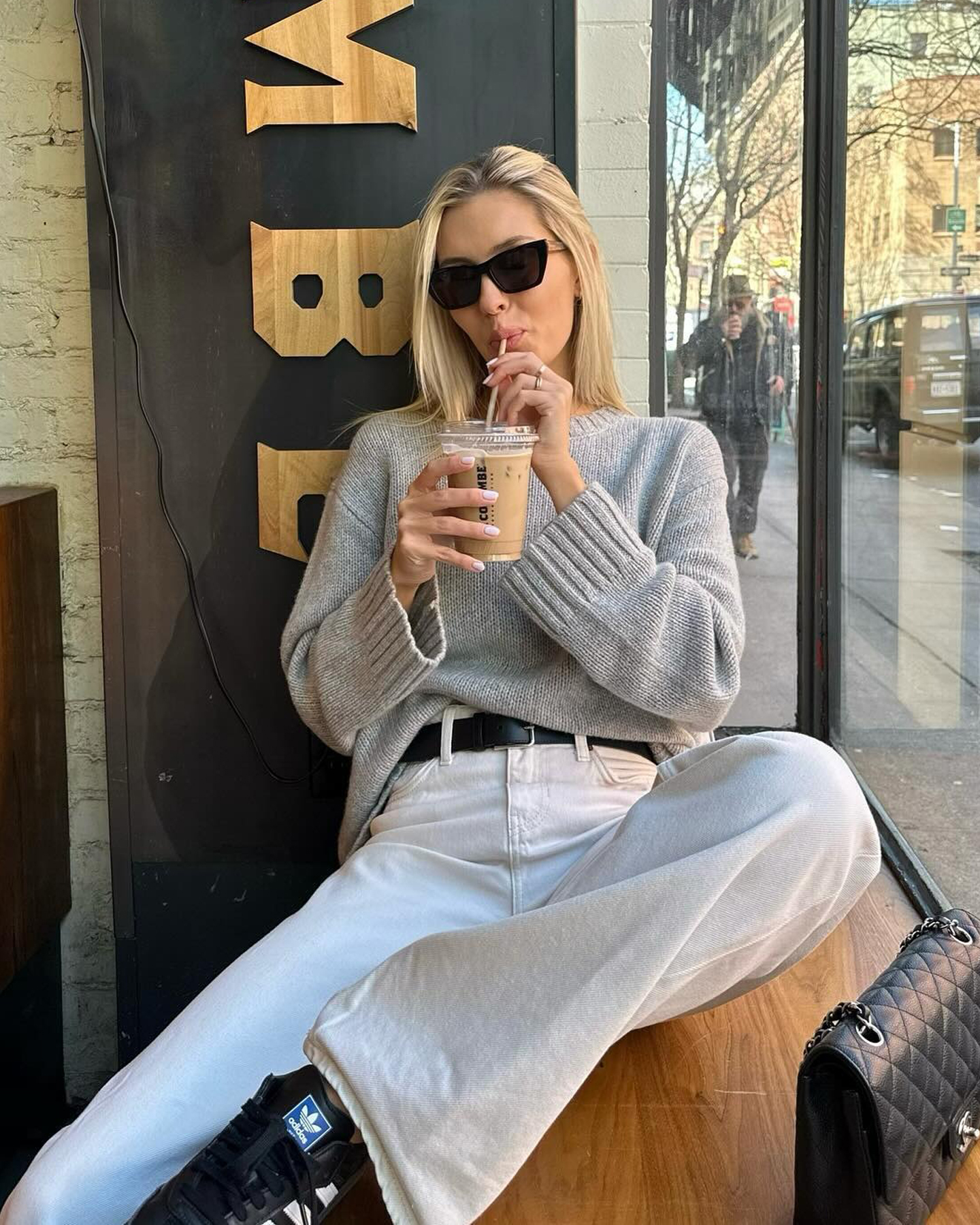 style influencer Fredrik Galgano wearing a black cat-eye sunglasses, a light gray oversize sweater, black belt, baggy white jeans, and black Adidas Samba sneakers