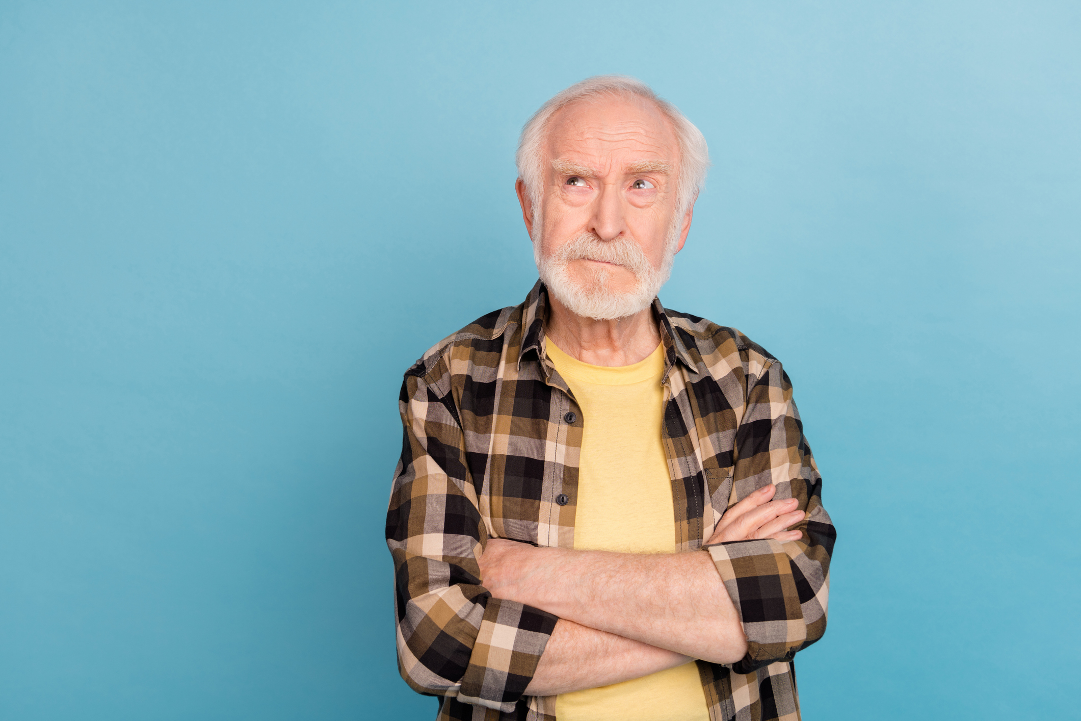 Photo of unsure funny retired man wear plaid shirt arms folded looking empty space isolated blue color background.