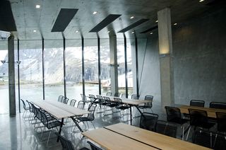 Interior view of the Trollstigen Visitor Centre featuring dark coloured walls, spotlights, floor-to-ceiling windows, pillars, wooden tables and black chairs