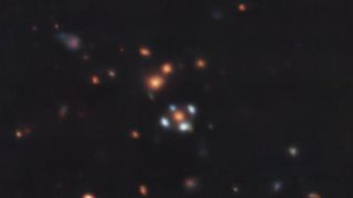 blurry dots against the blackness space are galaxies, with five in the center forming the shape of a blue, four-pedaled flower. the middle galaxy of the flower is red.