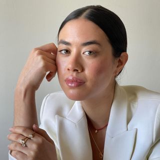 Sasha Mei wearing a white blazer and resting her hand on her face