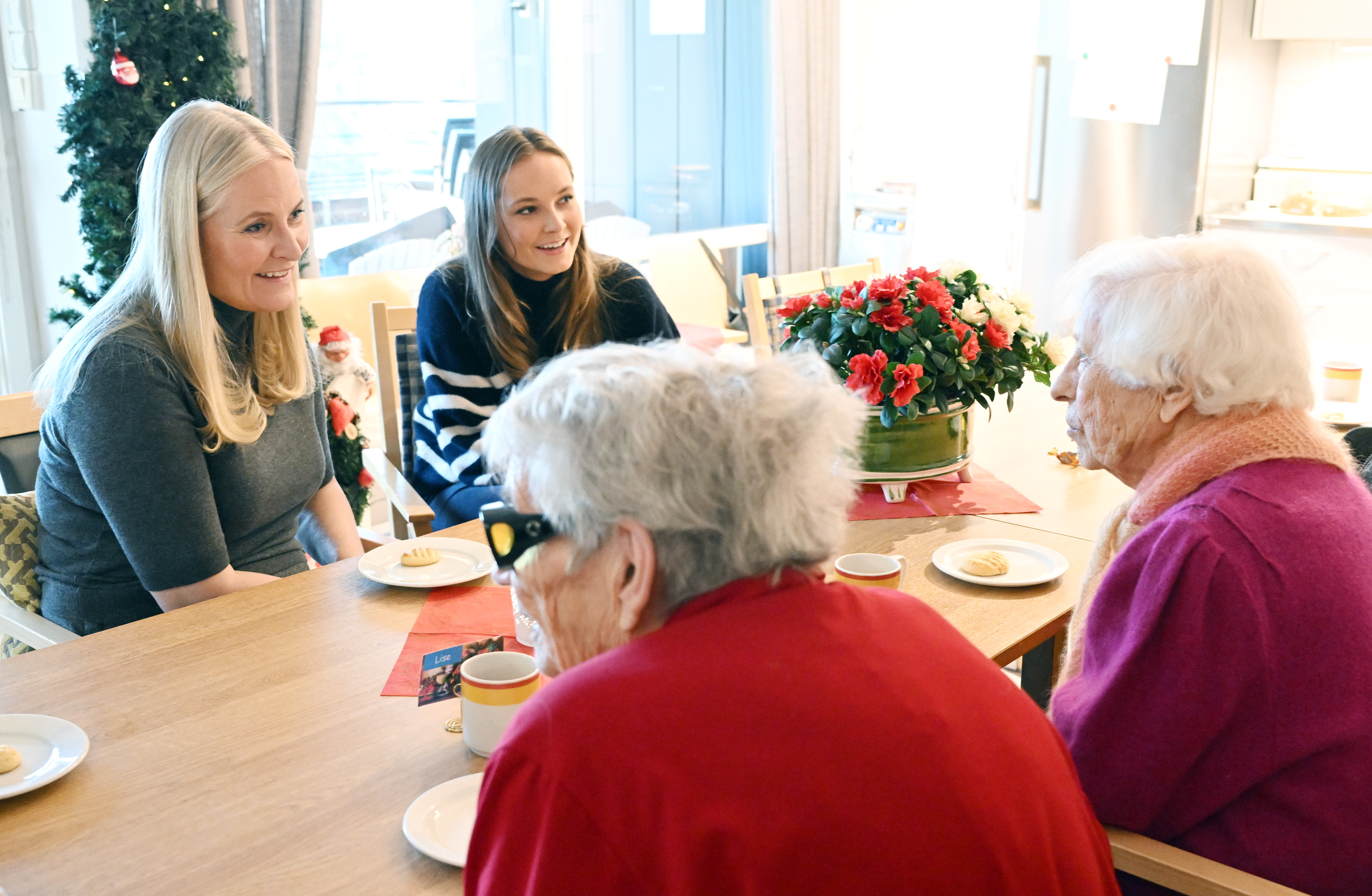 Crown Princess Mette-Marit sitting with Princess Ingrid Alexandra and two women at a table