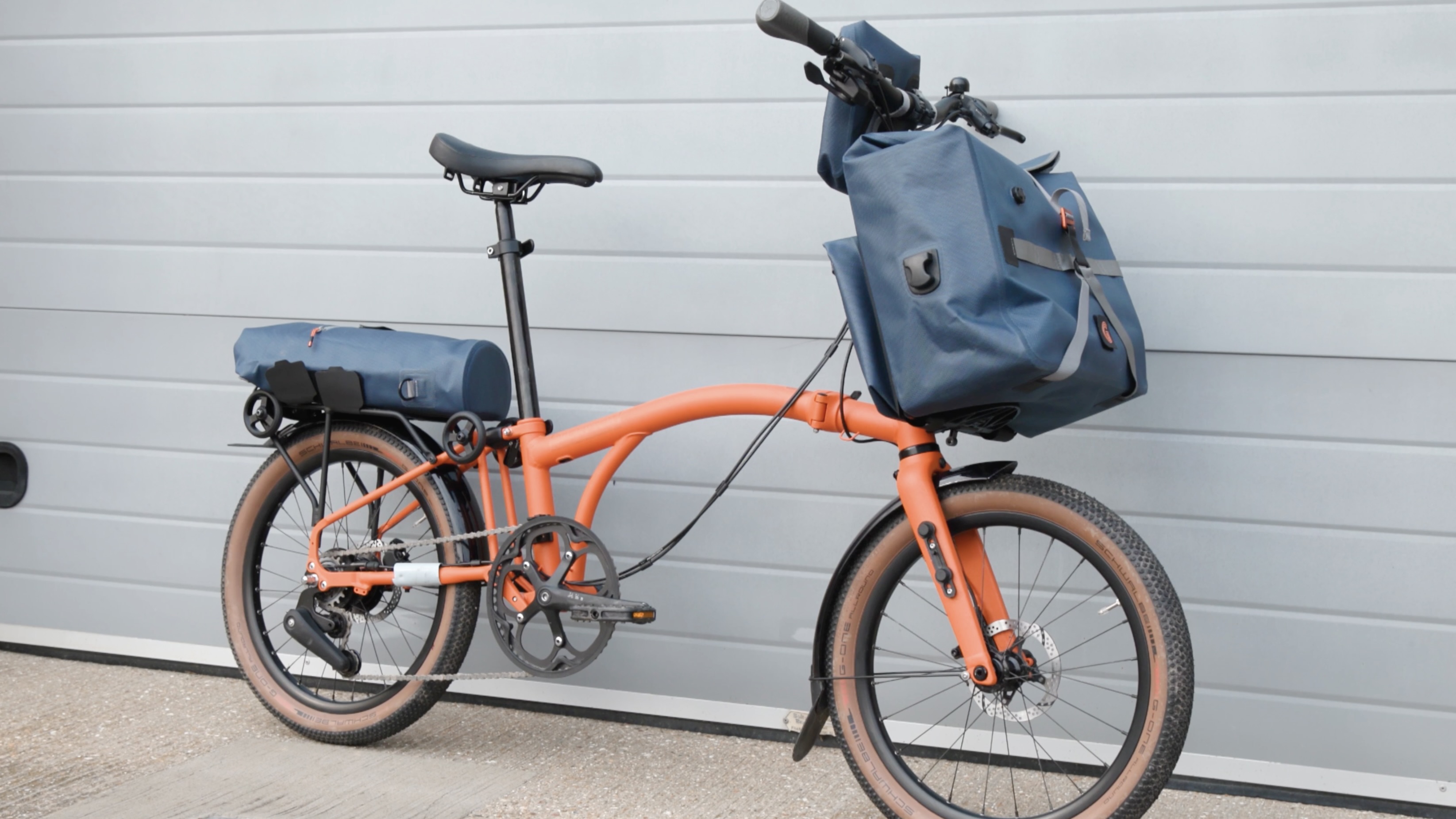 An orange Brompton covered in mud on a light gravel track