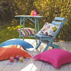 Blue painted wooden chair and table with coloured cushions on wooden decking area in garden