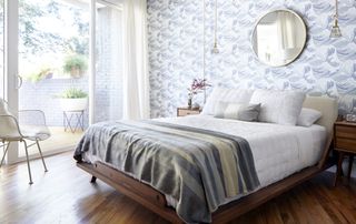 bedroom with blue wave wallpaper, blue stripe blanket, large mirror, side table, chairs, view to patio