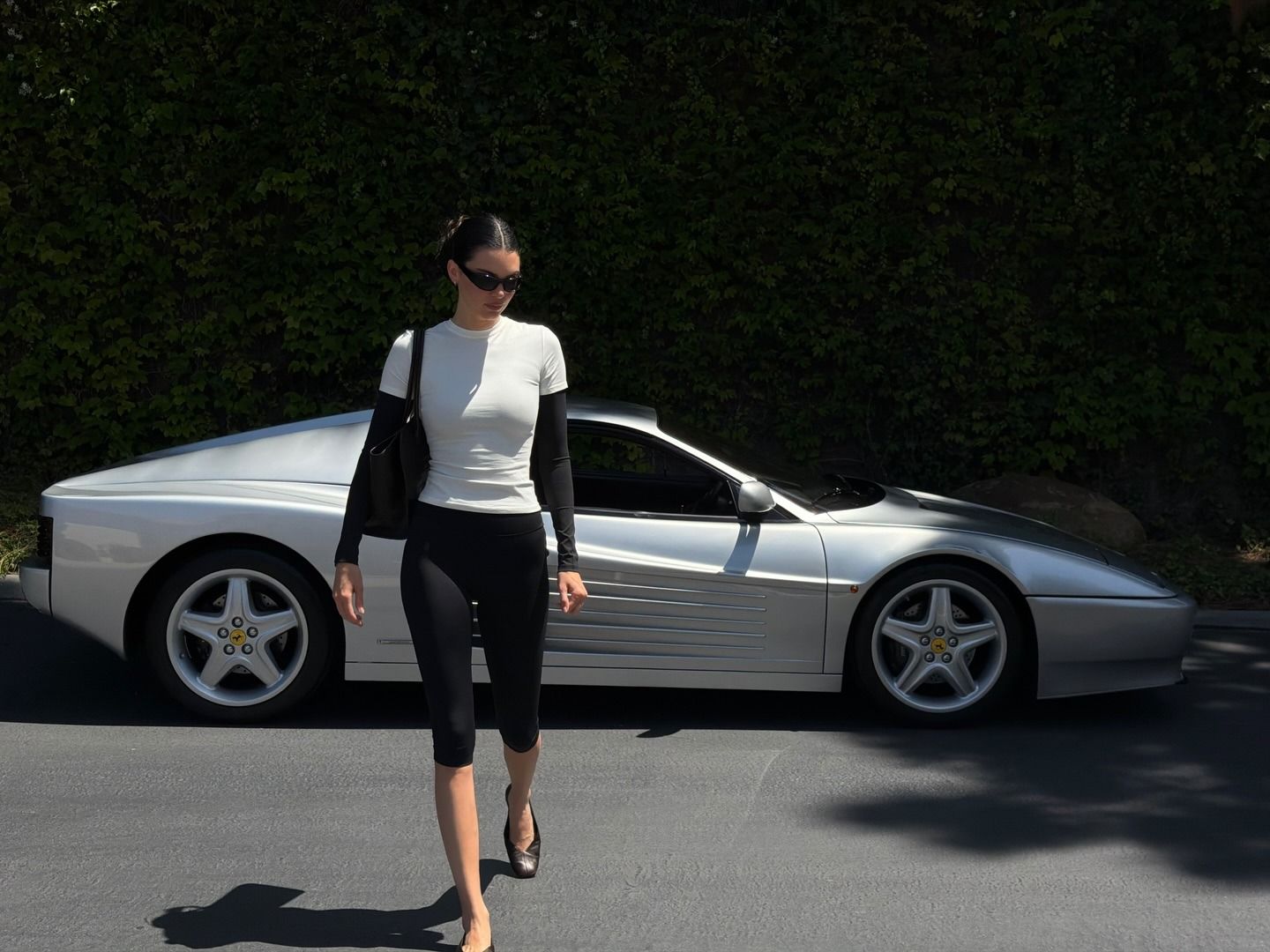 Kendall Jenner posing next to her vintage Ferrari 512 TR sports car wearing an Adanola layered T-shirt and capri leggings with The Row flats.