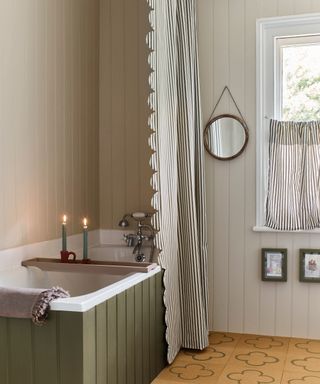 Classic gray bathroom with pale gray shiplap walls, striped fabric shower curtain and blind, olive green bath, cork floor,