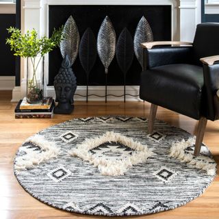 A gray aztec round rug sits on a wooden floor next to a black chair