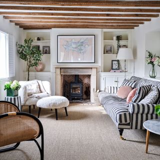 Brown carpet in cottage living room with wooden beams, stripe sofa and stone fire place