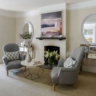 White fire place area with two grey one seater couches next to round coffee table
