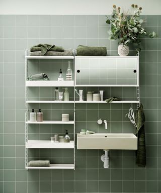 Modular shelving unit in white by String Furniture. Shelf positioned over small sink, toiletries and towels stored on the shelf, cabinet design with mirrored doors