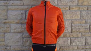 A rider wearing the Assos Equipe RS Rain Jacket Targa in an orange colorway