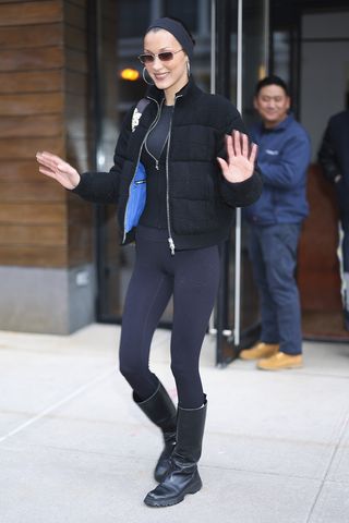 Bella Hadid wearing a puffer, leggings, and boots in NYC