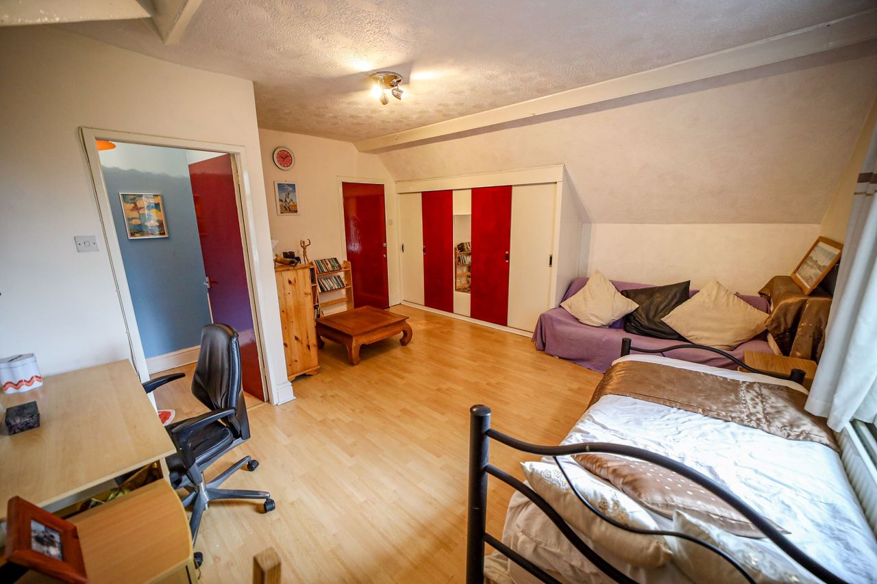 A dormer bedroom with wooden panelled flooring and a desk