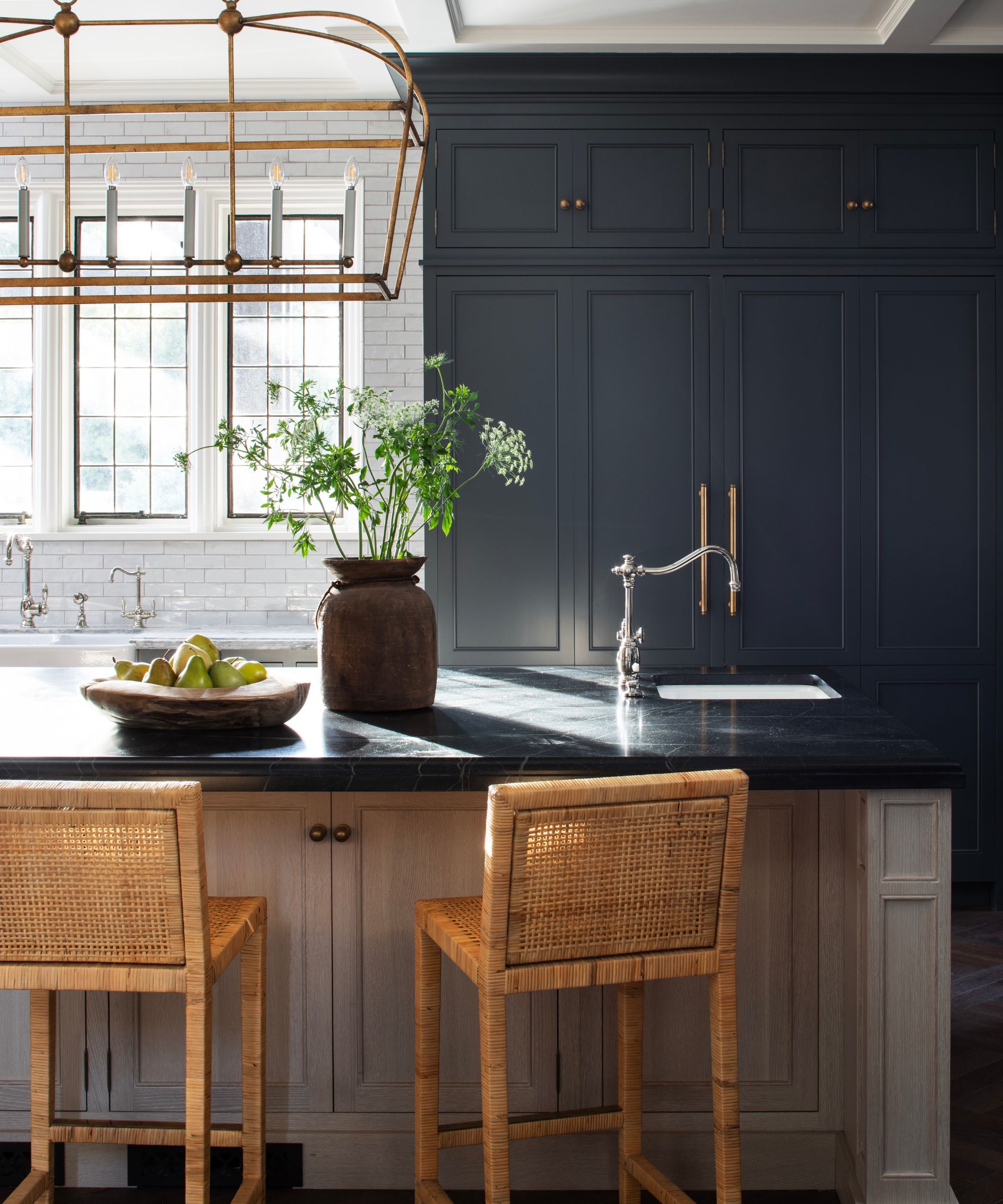 Dark gray kitchen with white subway tile backsplash and white countertops, with an island in light beige and a darker countertop and statement light above