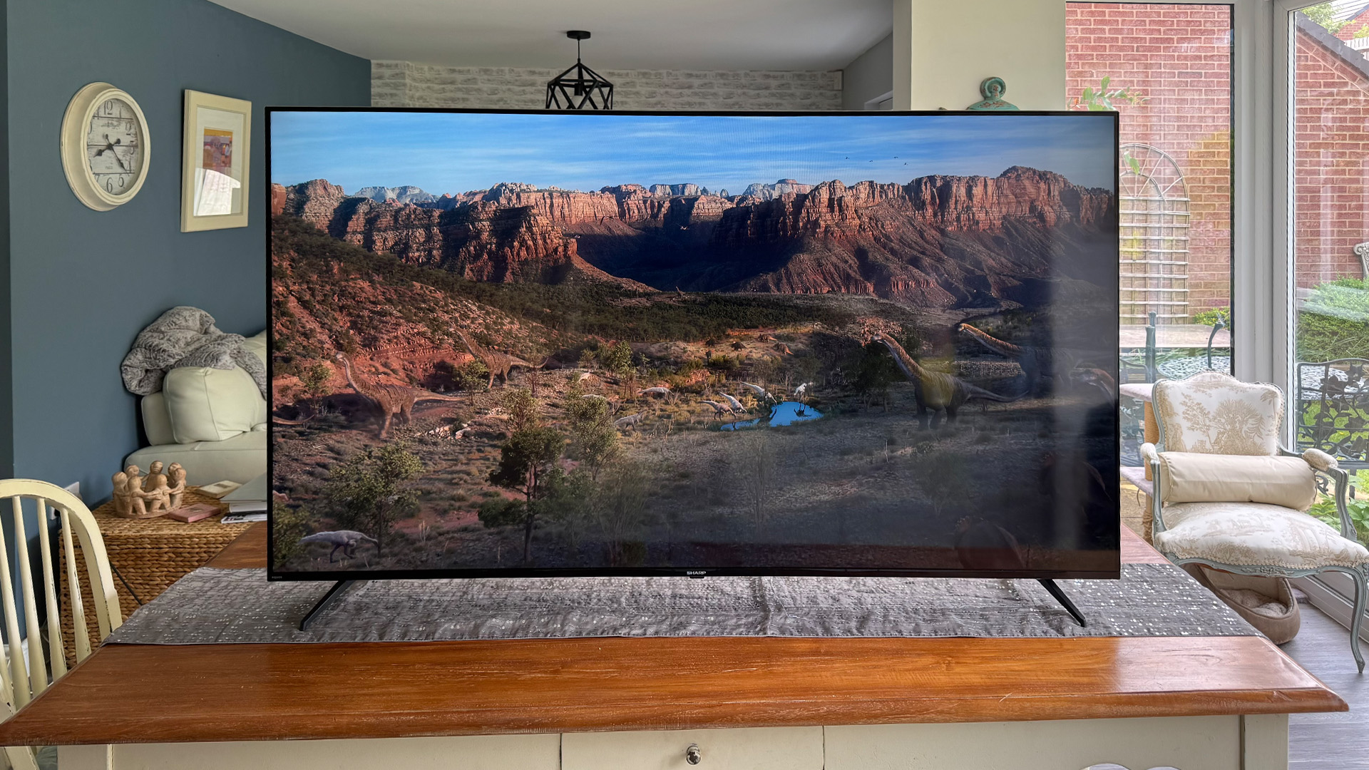 Sharp GK4245K 70-inch 4K TV on wooden dining table, on screen is lake and mountain view
