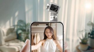 A hand holds a smartphone featuring a unique, motorized gimbal camera module on top that is pointed toward a woman displayed on the screen.