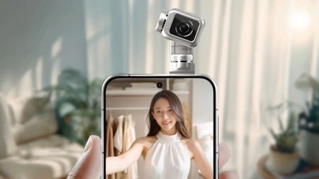 A hand holds a smartphone featuring a unique, motorized gimbal camera module on top that is pointed toward a woman displayed on the screen.