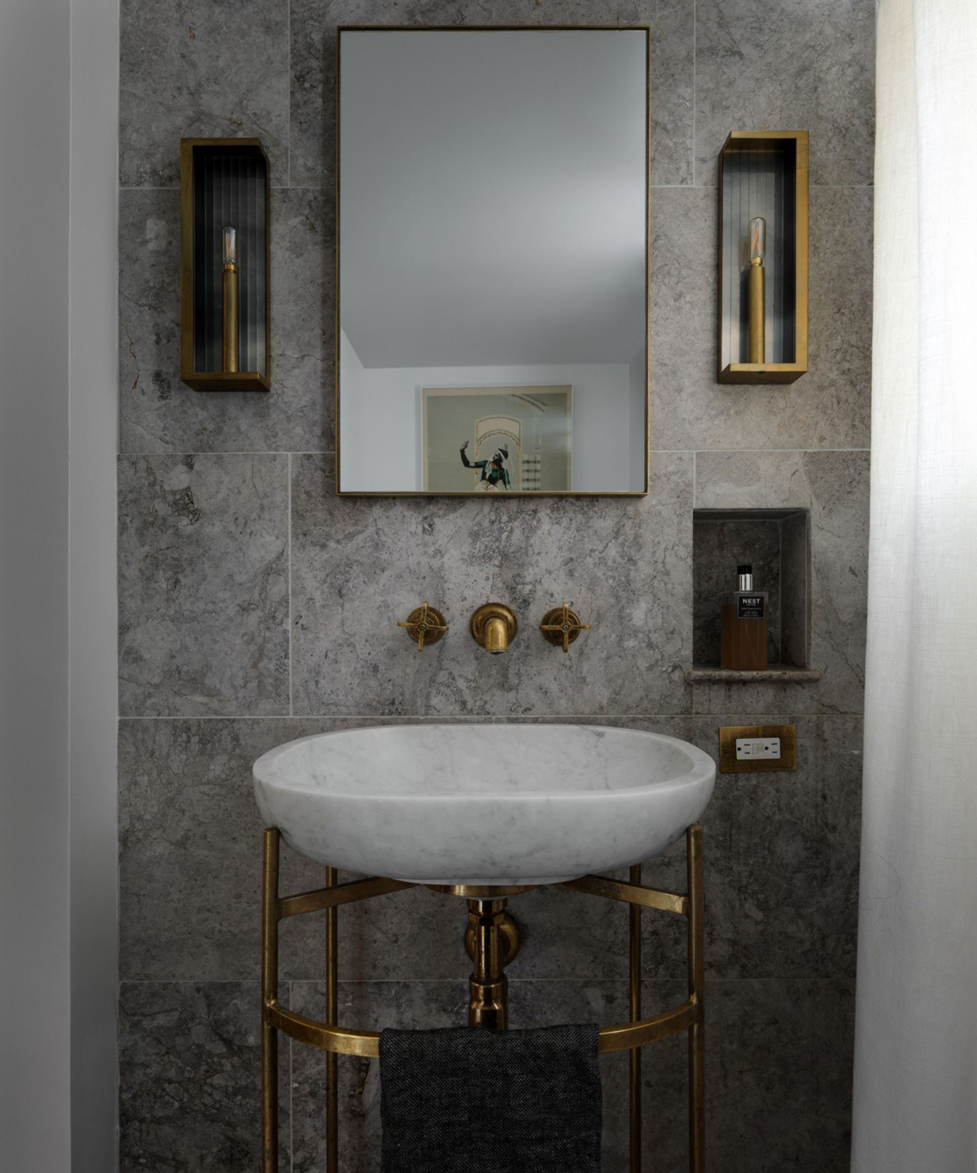 A small, moody bathroom with a statement marble sink on top of a gold metal stand