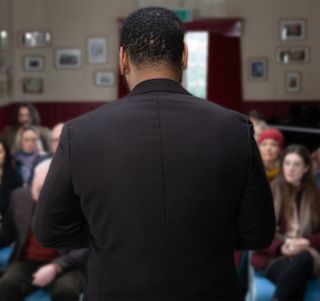 Village vicar Charles addresses the villagers during a vigil in the village hall