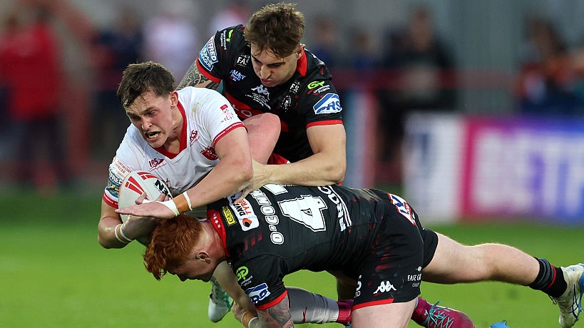 Jack Broadbent of Hull Kingston Rovers is challenged by Shea O'Connor and Finn McMillan of Wigan Warriors during the Betfred Super League match on May 21, 2026. 