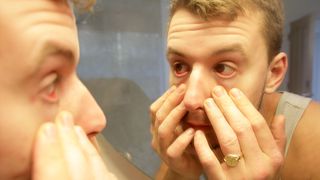 young man leaning into a mirror and pulling down on his eyes as if to inspect them