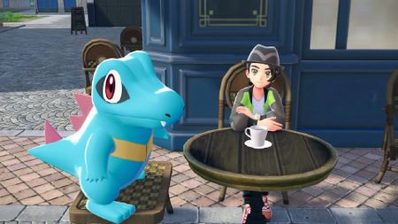 The player character in Pokemon Legends: Z-A sits next to an Alpha Totodile in front of a cafe