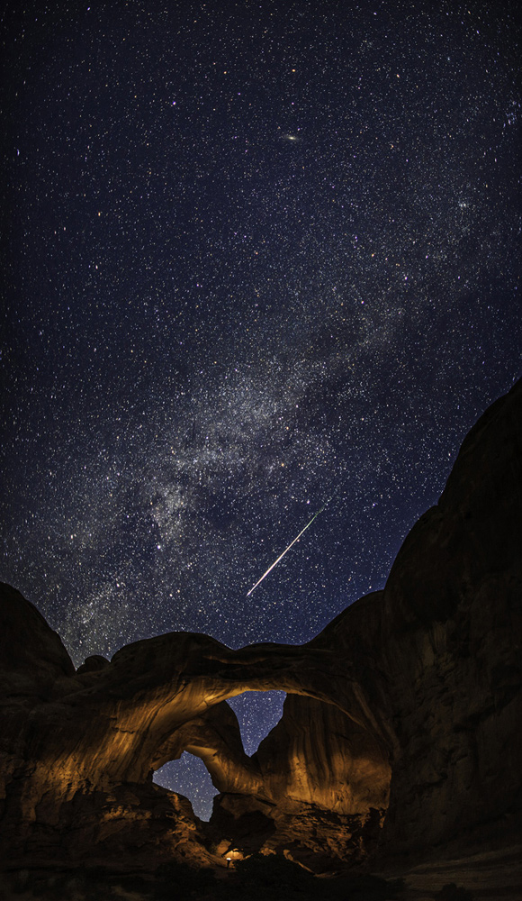 A bright streak reaches down through the sky towards natural stone arches 