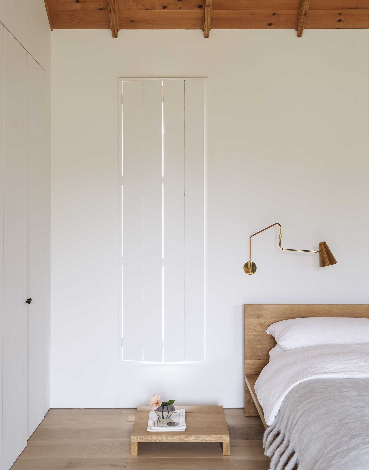 white beach house bedroom with wood floors, slender windows and modern shutters