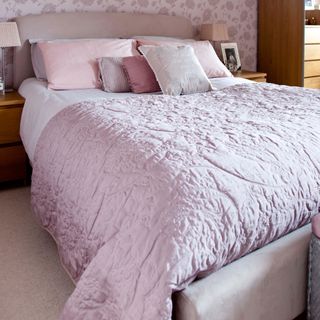 A bed with pink bedding matching pink floral wallpaper
