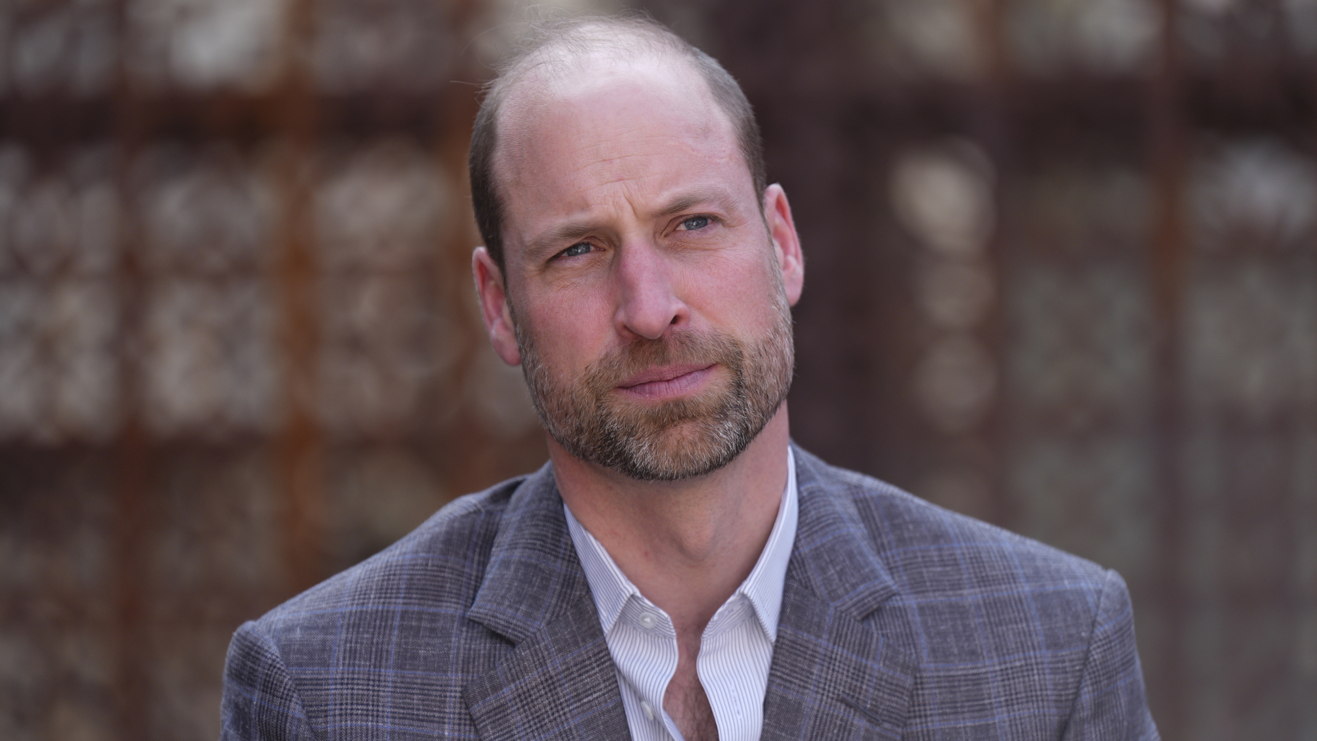 Prince William wears a gray plaid suit and a white suit and looks pensive