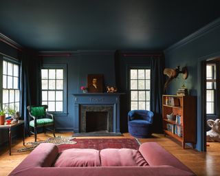 A small living room with a room painted dark green, juxtaposed by a pink and blue sofa