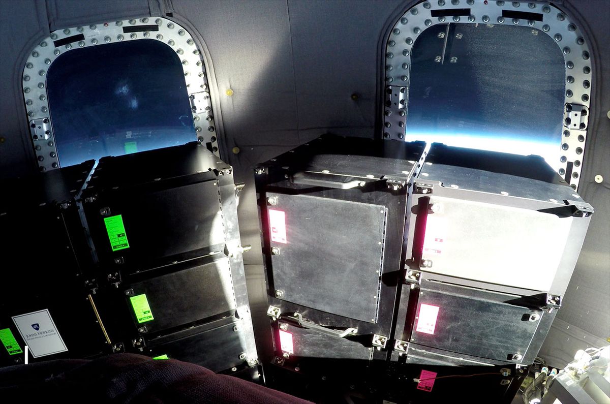 The blue haze of Earth&#039;s horizon glows through the windows behind payload racks aboard a Blue Origin New Shepard capsule in space. An auction benefiting SPACE on Ryder Farm is offering to fly an item of the winner&#039;s choice on a New Shepard flight.