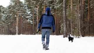 A man walking in the snow with his dog wearing jeans