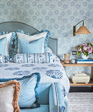 blue bedroom with patterned wallpaper, blue bed, patterned blue bolster cushions and throw and blue end of bed sofa